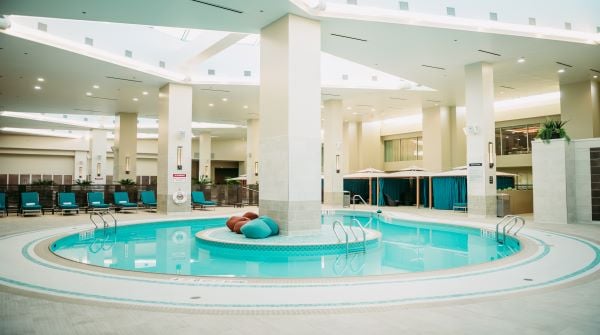 One of the main amenities of our hotel is our circular Indoor pool surrounded by blue lounge chairs and cabanas with multiple ladders for swimming safely.