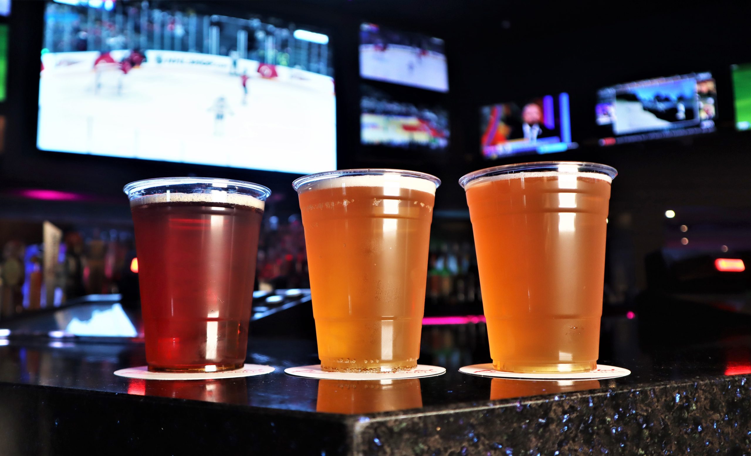 3 cups of beer with tv screens behind them