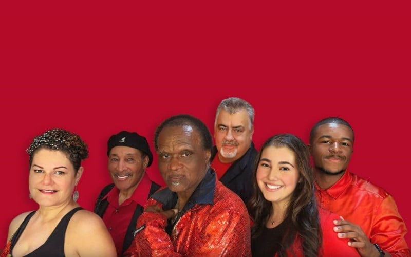 6 people standing next to each other in front of a red background