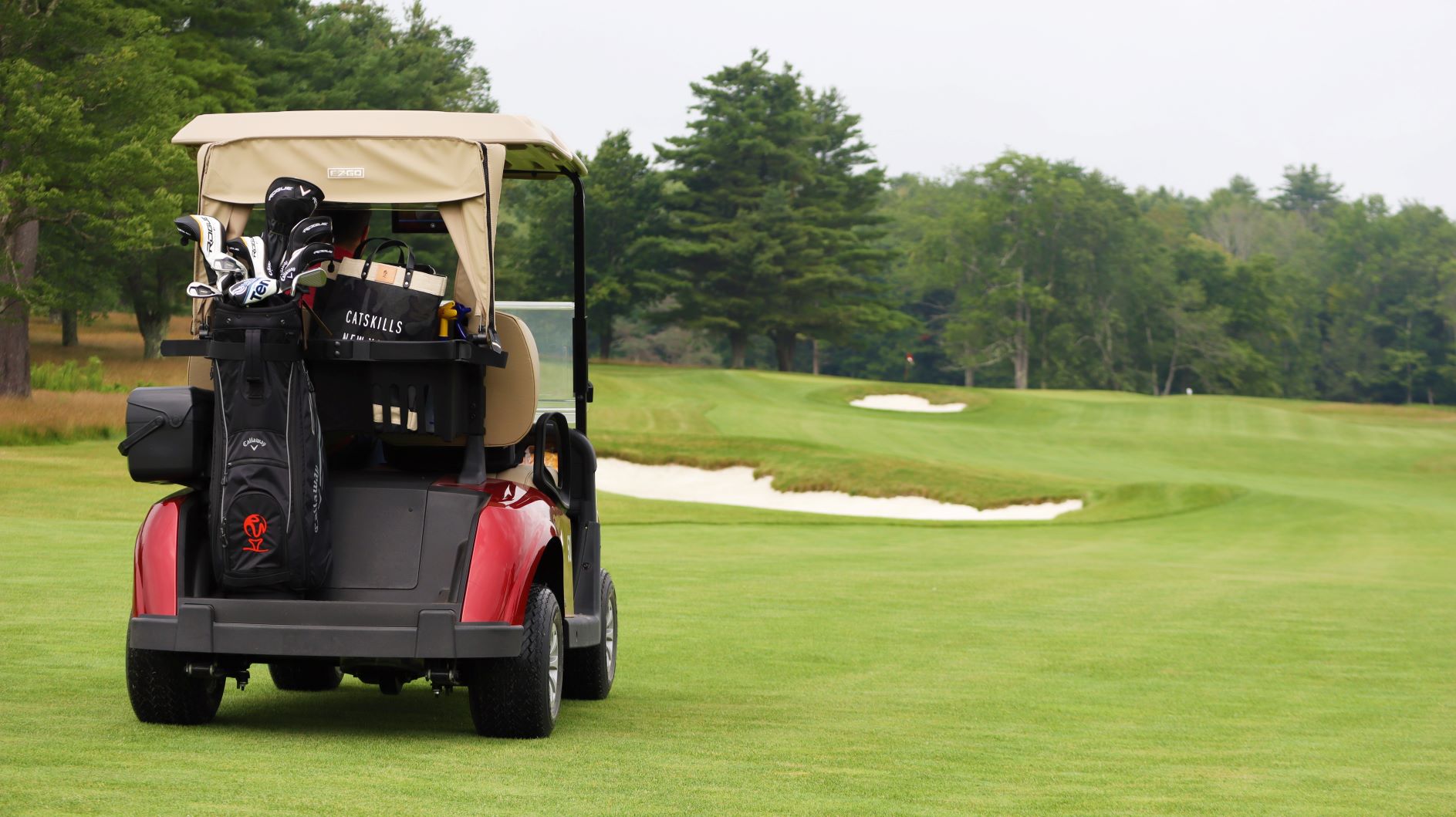 Monster golf club golf cart approaching a sand trap with the green in the distance. A monster golf club golf bag is attached to the back