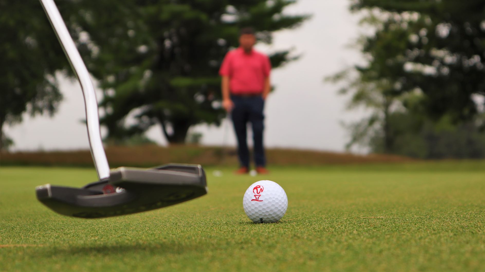 Close up on Monster golf club logoed golf ball with a golf putter in motion behind it