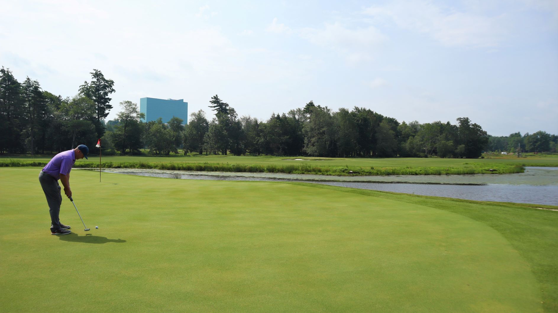 Golfer putting on a green on a body of water with Resorts World Catskills Tower visible in the background