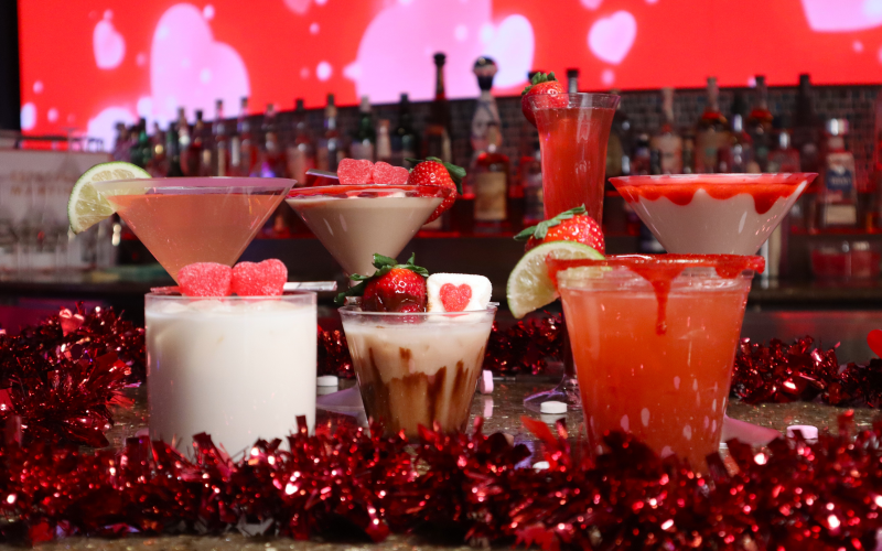 Seven Valentine's Day themed cocktails in front of a screen with hearts